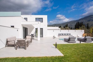 Ein modernes Haus mit Terrasse, Sitzgelegenheit im Freien und einem Pool.