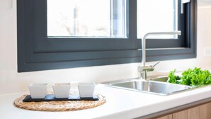 A kitchen with a modern faucet, a window with a dark frame, and a woven placemat with three white cups. - Amalfi Twins Villa A (Nydri)