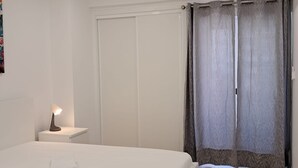 Ett sovrum med en säng, ett nattduksbord med en lampa, en garderob och ett fönster med gardiner.