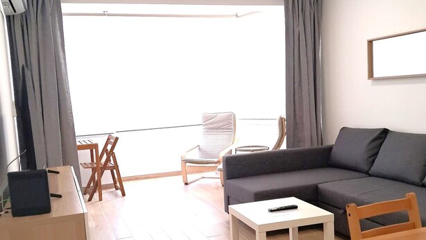 Ett modernt vardagsrum med en soffa, ett soffbord, ett skrivbord med en bärbar dator och en balkong med en stol.