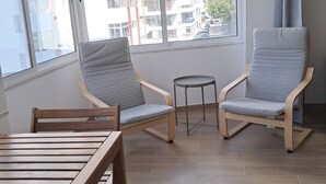 En balkong med två stolar, ett litet bord och utsikt över stadsbilden.