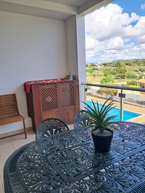 Ein Balkon mit Blick auf einen Pool, einer Holzkommode, einer Bank und einem Tisch mit Stühlen.