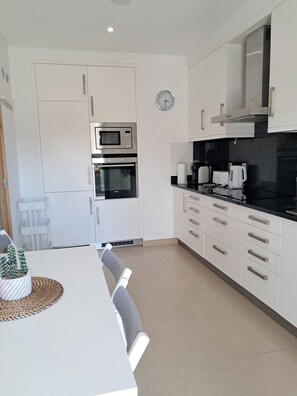 Eine moderne Küche mit weißen Schränken, einer Mikrowelle, einem Backofen und einer Wanduhr.