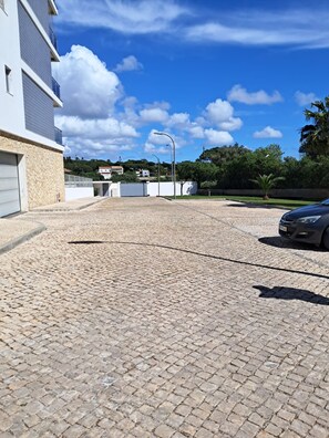 Ein gepflasterter Weg führt zu einem Gebäude mit Garage, einem geparkten Auto und blauem Himmel mit Wolken.