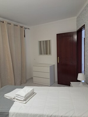 Ein Schlafzimmer mit Bett, Kommode, Tür und Fenster.
