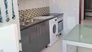 A compact kitchen with a washing machine, a sink, and a dining table. - T2 VISTA MAR in Quarteira (Quarteira)