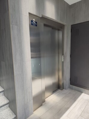 Ein moderner Aufzug mit einem Warnschild, einer Treppe und einer schlichten Tür.
