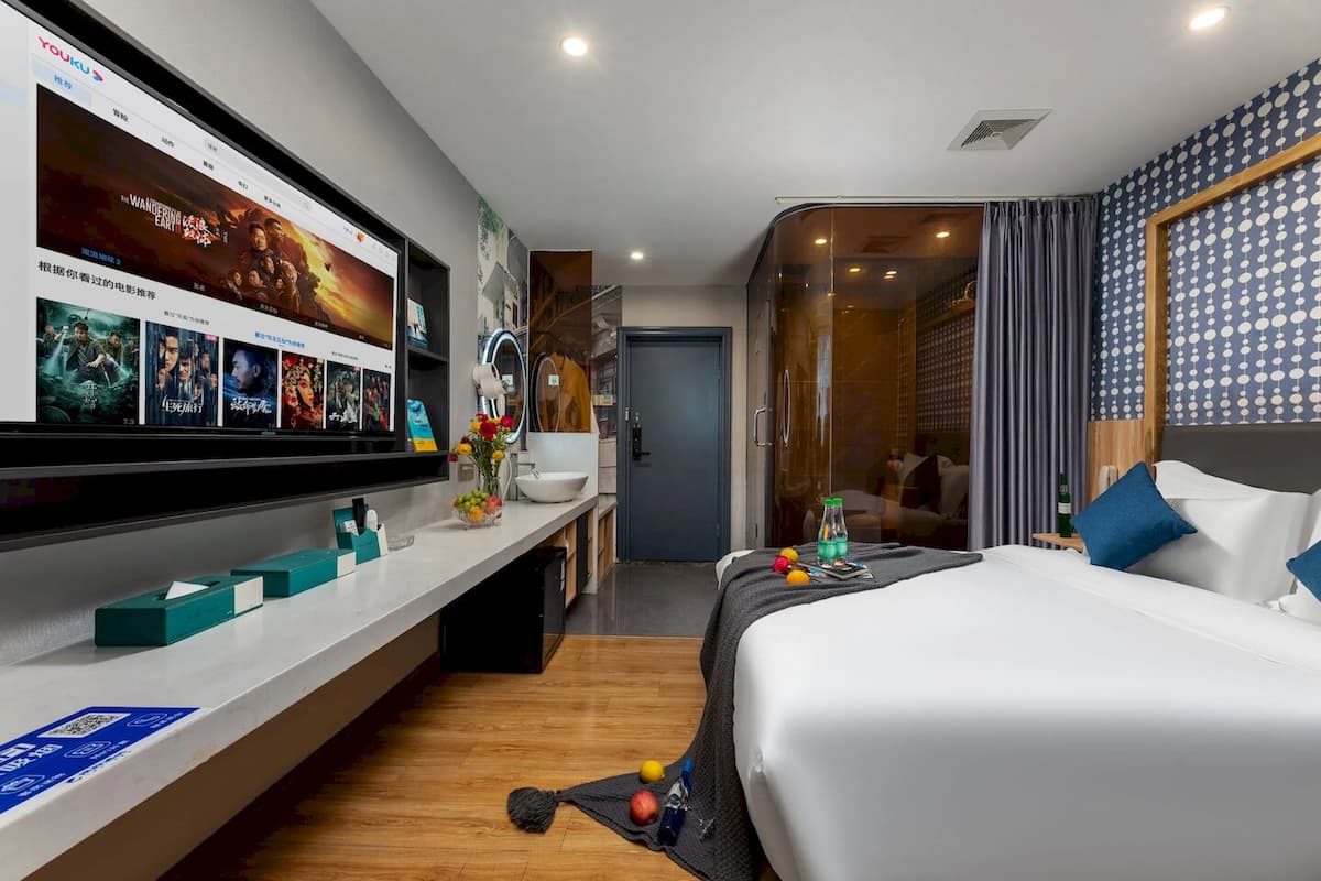 A hotel room with a bed, a desk with a computer, a mirror, and a wall with movie posters.