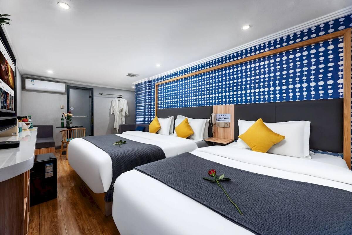 A hotel room with two beds, a desk, a wardrobe, and a wall with a polka dot pattern.