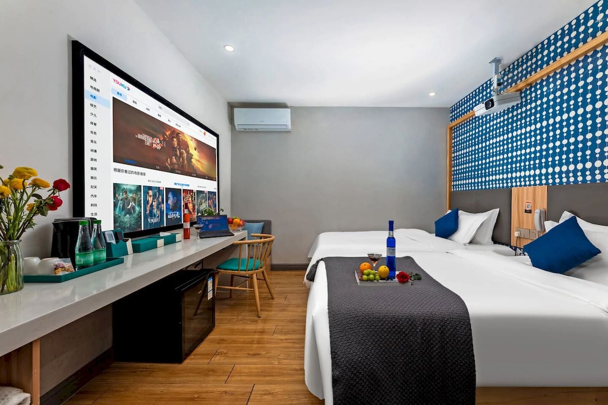 A hotel room with a bed, a desk with a computer, a chair, and a wall-mounted TV.