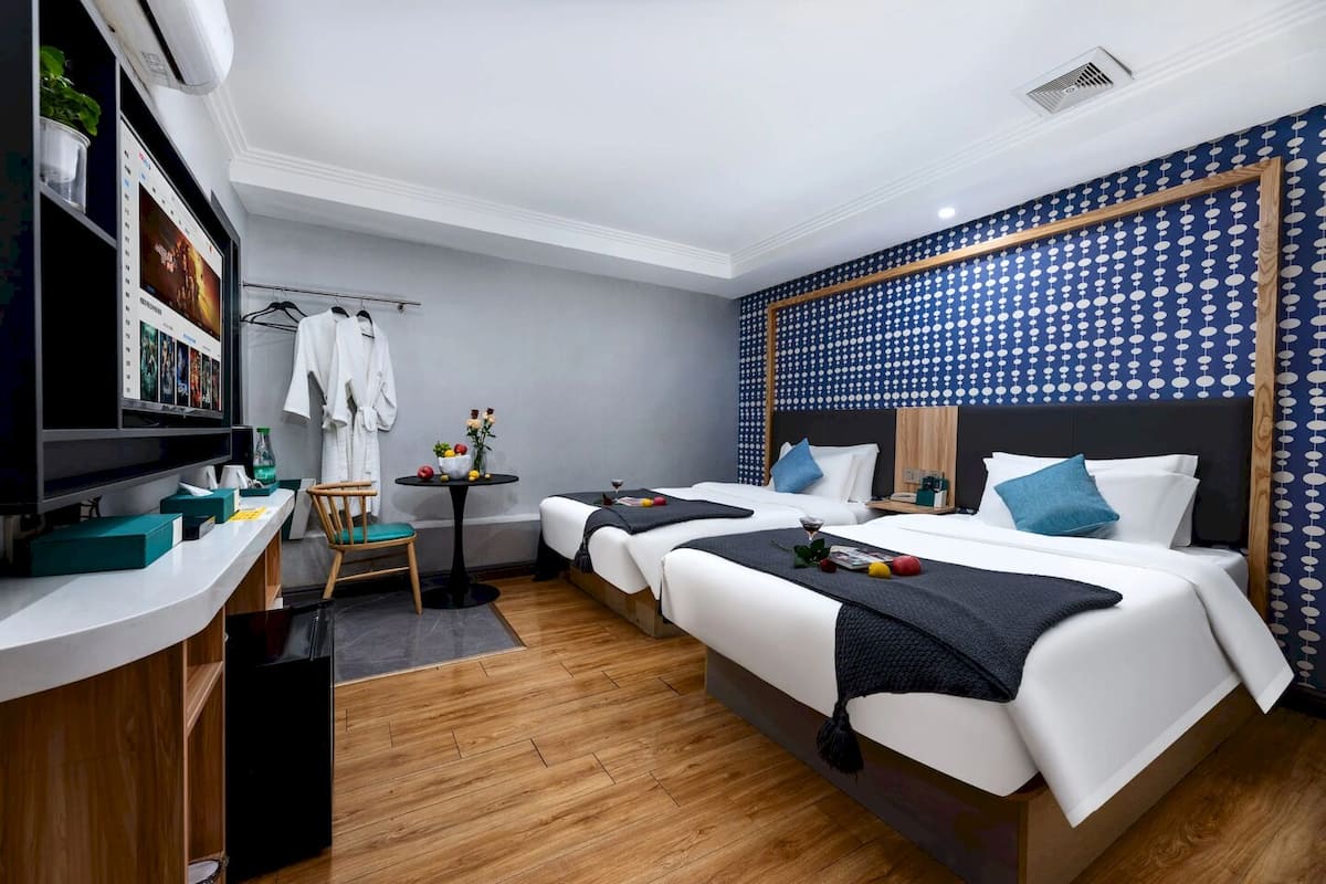 A hotel room with two beds, a desk with a computer, a chair, and a small table with a vase of flowers.