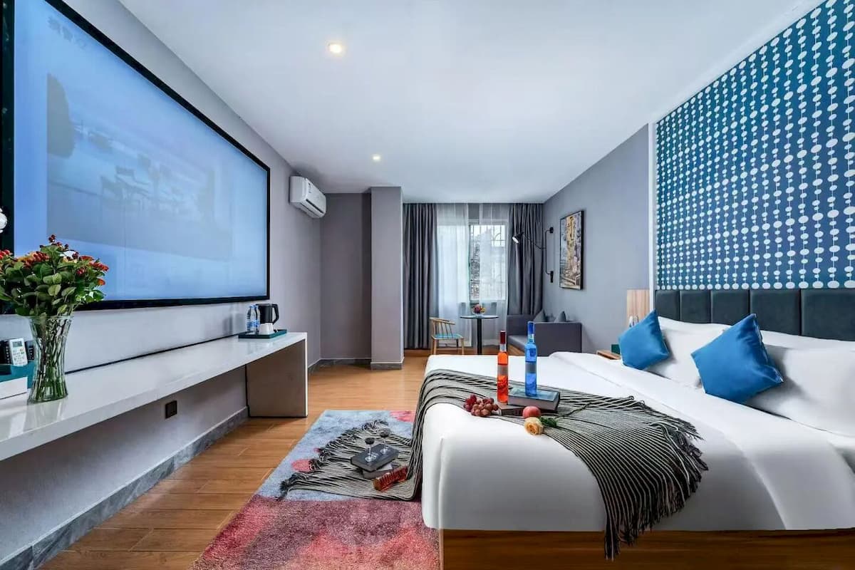 A modern hotel room with a large bed, a flat-screen TV, a desk with a coffee maker, and a large window.