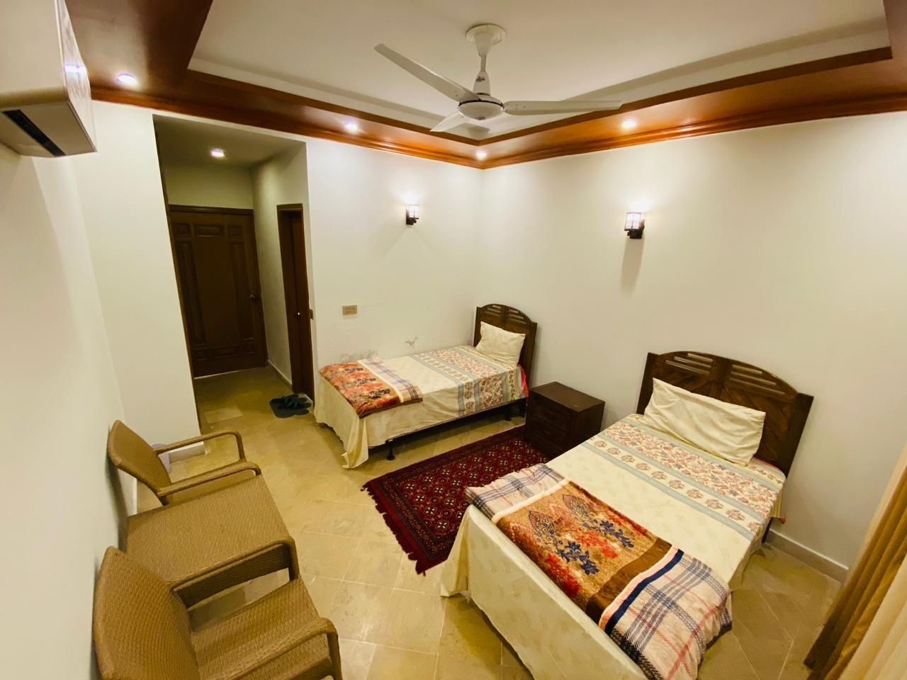A bedroom with two single beds, a ceiling fan, and a small seating area.