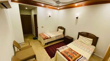 A bedroom with two single beds, a ceiling fan, and a small seating area.