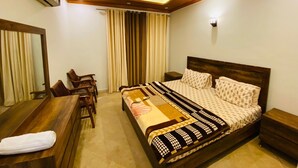 A hotel room with a bed, a desk, a chair, a ceiling fan, and a window with curtains.