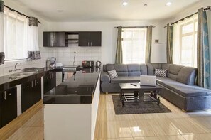 Une cuisine moderne dotée d’un îlot central, un coin repas avec un canapé et une table basse, et un espace de vie avec un divan et un ordinateur portable.