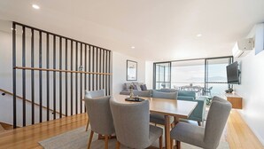 Una sala de estar moderna con comedor, una escalera y un ventanal con vistas.