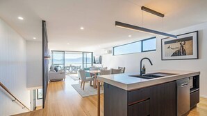 Una cocina moderna con una isla central, un comedor con vistas y una escalera que sube a un piso superior.