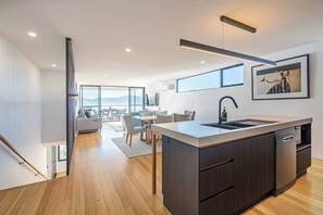 Et moderne køkken med en central ø, et spiseområde med udsigt og en trappe til en etage ovenpå.