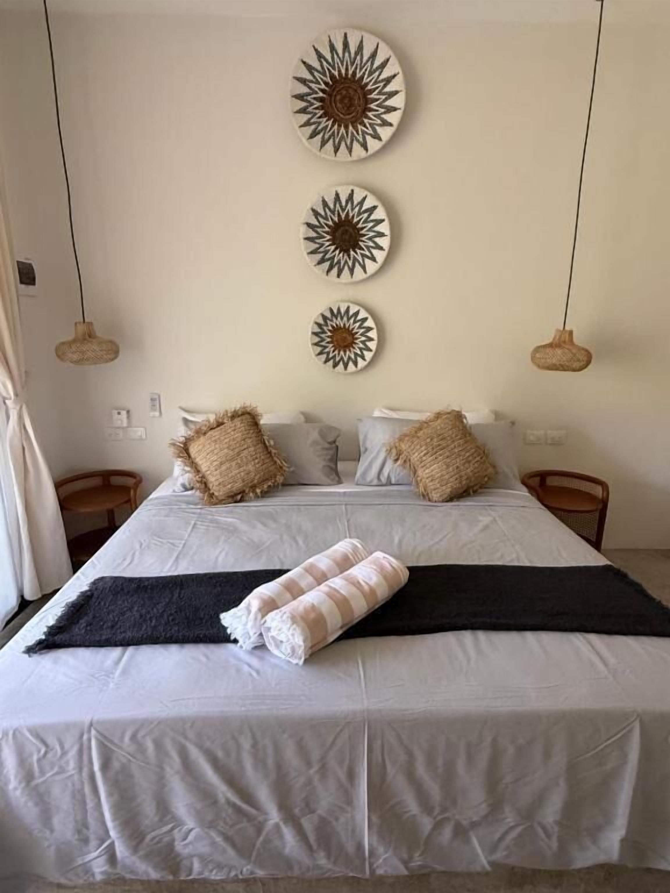 A bed with a white bedspread, two pillows, a black throw blanket, and three wall-mounted decorative plates.