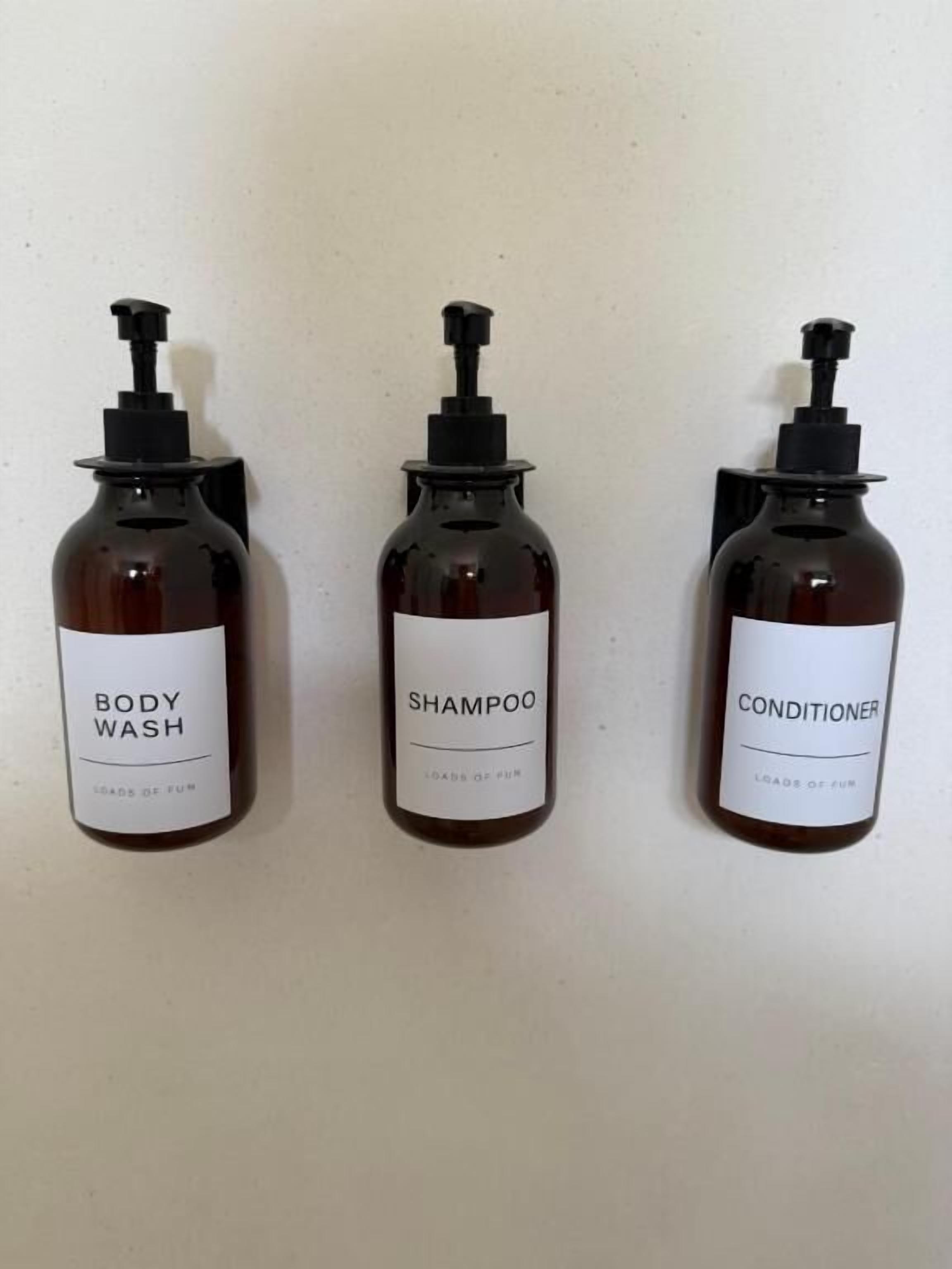 Tres botellas de líquido con dosificadores, etiquetadas 'BODY WASH', 'SHAMPOO' y 'CONDITIONER'.