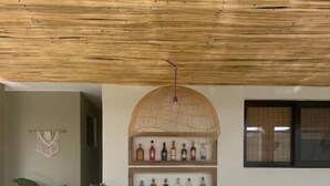 Eine moderne Küche mit Holzbalkendecke, einer zentralen Kochinsel mit Barhocker und einem Regal mit Flaschen.
