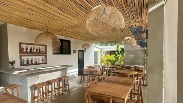 Ein Restaurant mit Holztischen und -stühlen, einer Bar und einer Decke aus gewebtem Material.