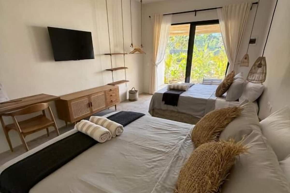 A modern bedroom with a bed, a desk, a television, and a ceiling fan.