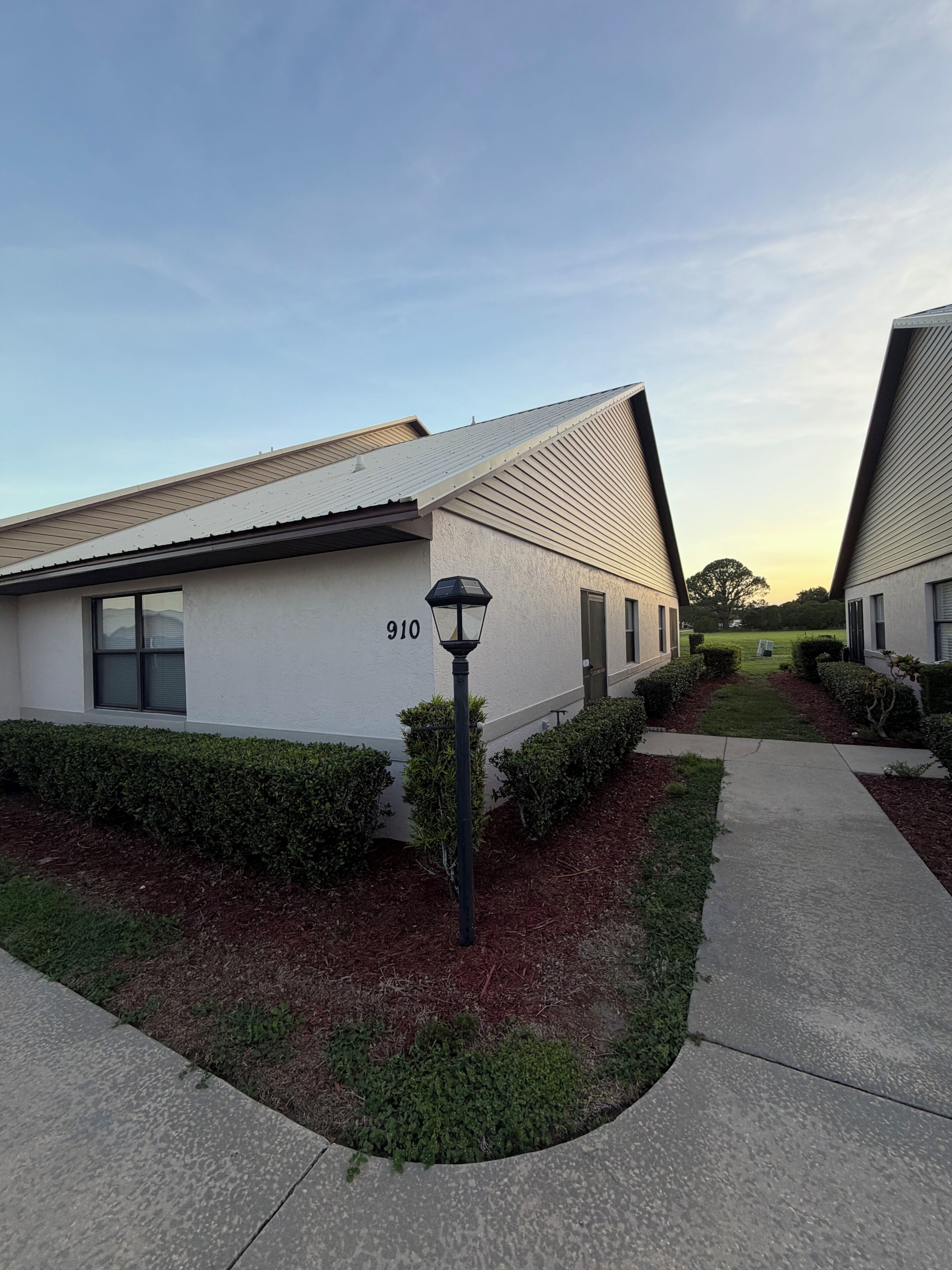A modern building with a flat roof, a number '910' on the side, and a well-maintained hedge.