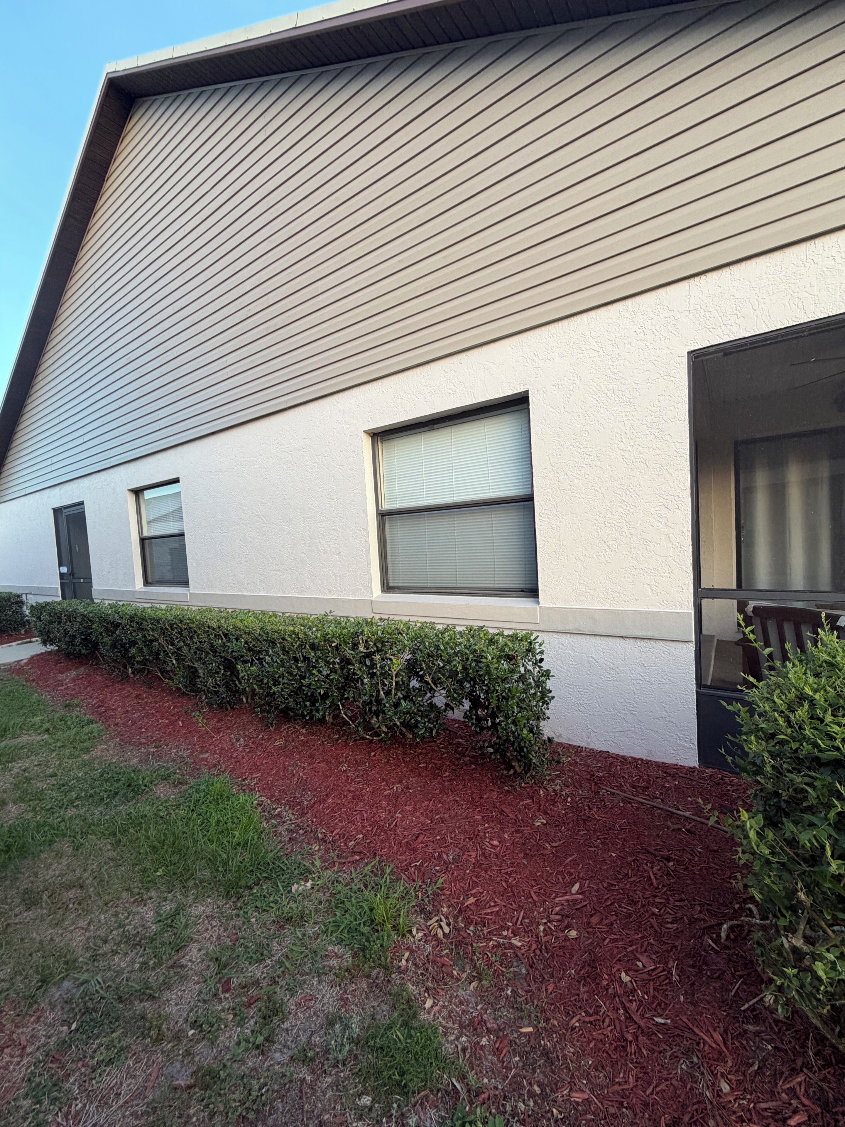 A building with a sloped roof, a window with blinds, and a well-maintained hedge.