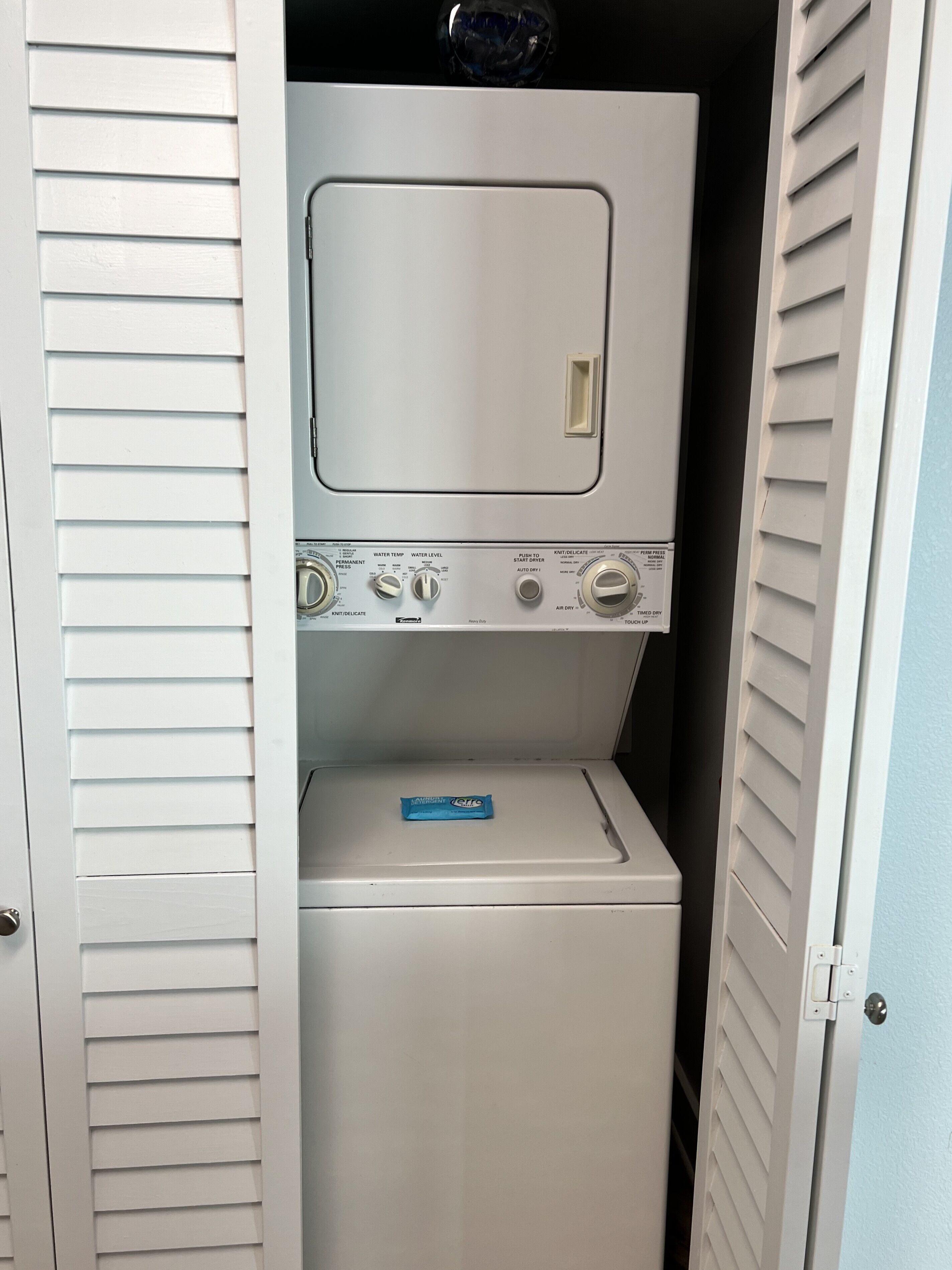 A laundry room with a front-loading washer and dryer, control knobs, and a blue detergent package on the dryer.