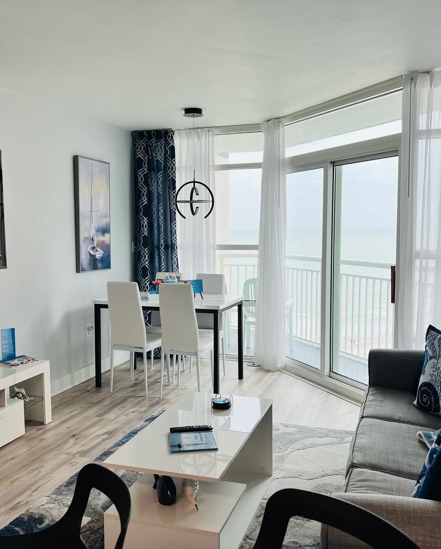 Sala de estar moderna com área de jantar, janelas amplas e vista para o mar.