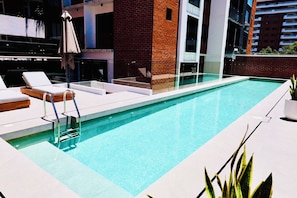 Ein moderner Pool im Freien mit Liegestühlen, einer Glasufernung und einer Backsteinmauer.