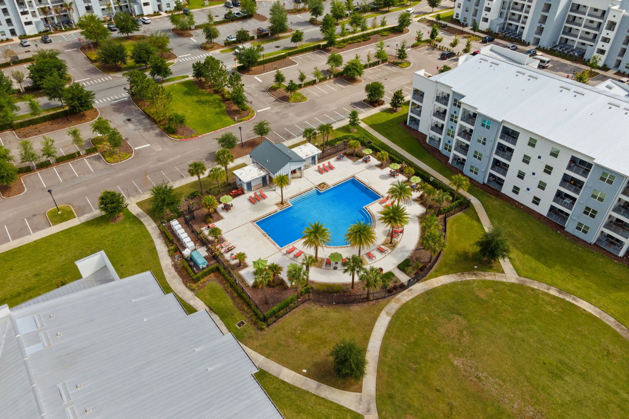 Vista aèria d'un complex residencial amb una piscina central, diverses places d'aparcament i vegetació als voltants.