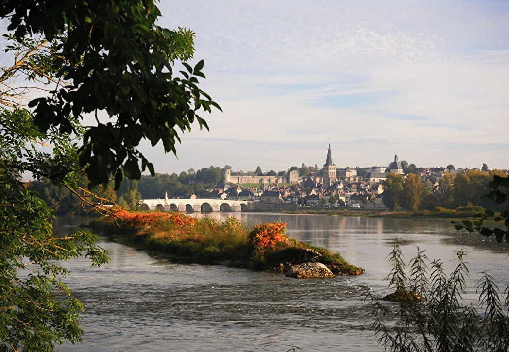 A river with a bridge, a town in the background, and a prominent church spire.