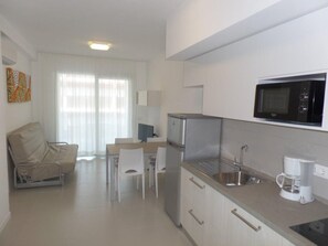 A compact kitchen with a microwave, coffee maker, and a refrigerator. There is a dining area with a table and chairs. - Sleek Modern Home With a Rooftop Pool (San Michele al Tagliamento)