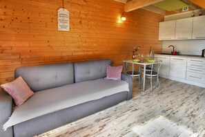 Een gezellige kamer met een grijze bank, een eettafel met stoelen en een keuken met witte kasten.