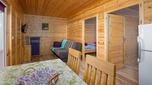Een houten hutje met een bed, een tafel met een bloemrijk tafelkleed, een stoel en een koelkast.
