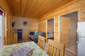 A wooden cabin with a bed, a table with a floral tablecloth, a chair, and a refrigerator. - Holiday homes, attractions for children (Rusinowo)
