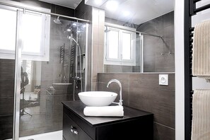 Un baño moderno con cabina de ducha de vidrio, un lavabo blanco y una toalla.