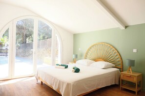 Un dormitorio con una cama grande, dos mesitas de noche, un cabecero redondo y un ventanal corredero que da a un área exterior.