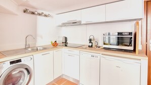 Ett kompakt kök med tvättmaskin, diskmaskin, mikrovågsugn och kaffebryggare.