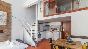 Ett kompakt bostadsutrymme med en säng, ett litet kök och en matplats med bord och stolar.