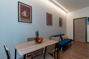 Ein modernes Zimmer mit Esstisch, Stühlen, Obstschale, einer Couch und gerahmten Bildern an der Wand.