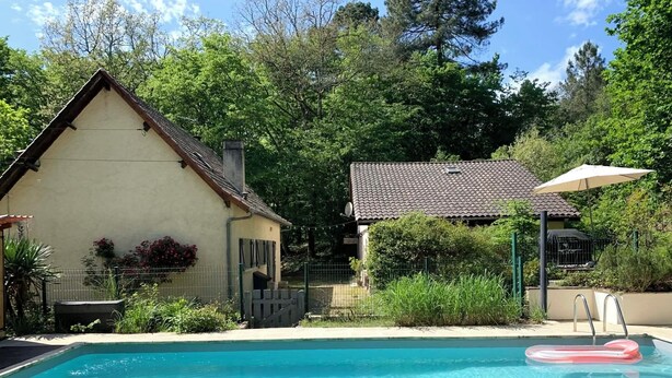 A swimming pool with a floating ring, a lounge chair, and a house with a tiled roof. - Small cottage in the woods with private pool (Saint-Jean-d'Estissac)