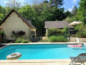 Une piscine avec un flotteur, un fauteuil de relaxation et une maison avec un toit en tuiles.