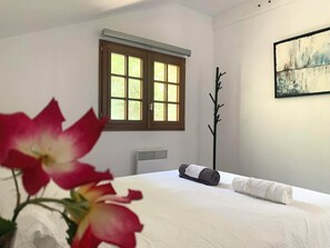 Quarto de hotel com cama, janela, radiador e um quadro na parede.