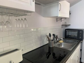 Uma cozinha moderna com um fogão por indução preto, um forno elétrico e uma pia de aço inoxidável.