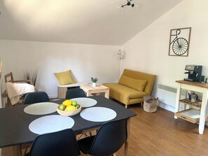 Un comedor con una mesa, sillas, un bol de fruta, un sofá, una cafetera y un radiador.