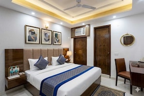 Quarto de hotel com cama, mesa de cabeceira, escrivaninha e uma secretária com cadeira.